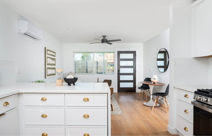 A modern, newly completed ADU interior featuring a bright white kitchen, gold accents, and an open-concept dining area.