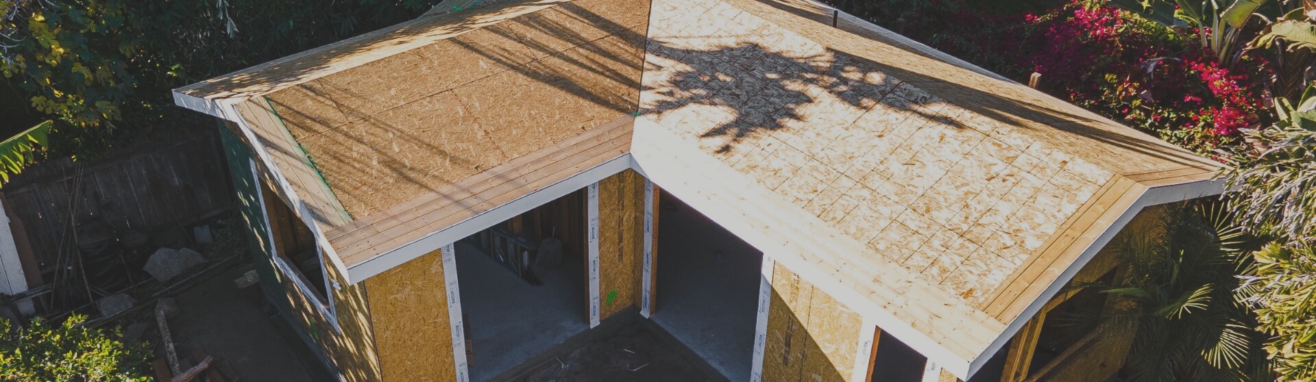 A top-down aerial view of a partially completed ADU with a finished roof, surrounded by lush greenery in San Marcos.