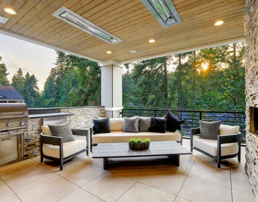 Covered porch with modern seating, integrated lighting, and a grill area in a scenic backyard setting.