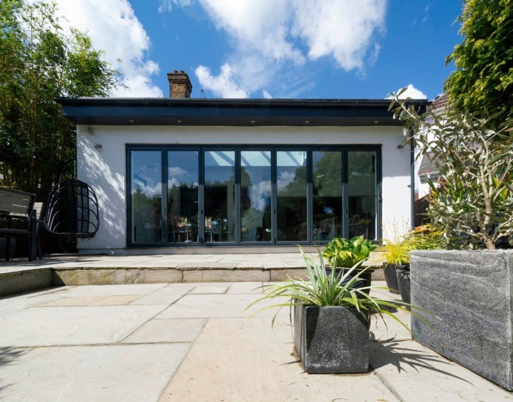 A modern patio featuring large sliding glass doors, surrounded by vibrant planters and a minimalistic seating arrangement.