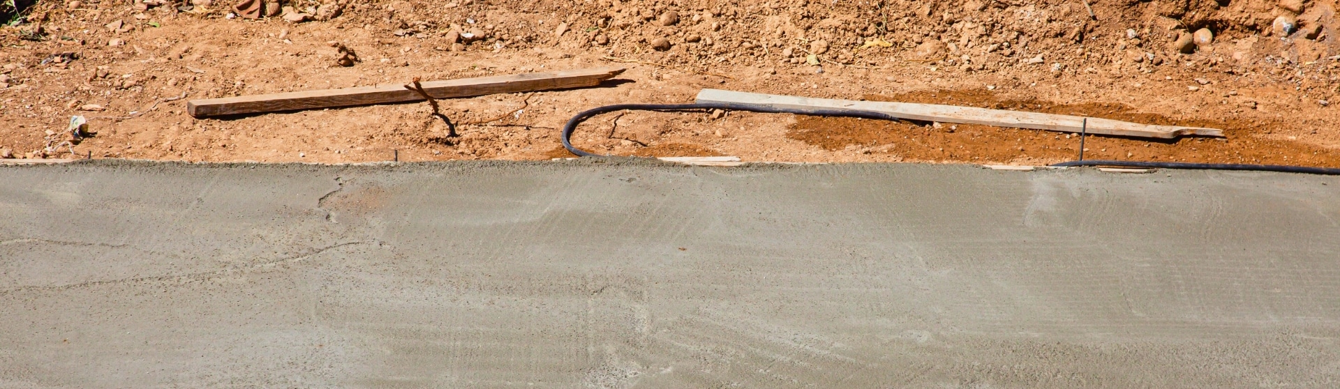 Close-up of a freshly poured ADU concrete foundation with dirt and tools nearby.