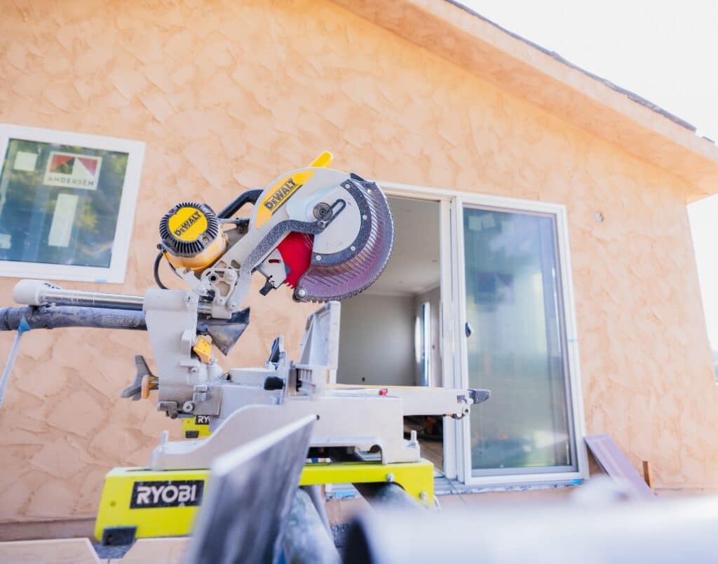 A close-up of a saw with a partially built ADU in the background.