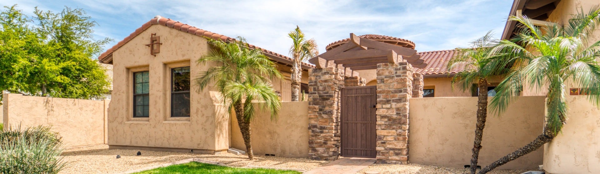 Spanish-style ADU with stucco walls, red tile roof, and a stone archway entrance surrounded by desert landscaping and palm trees.