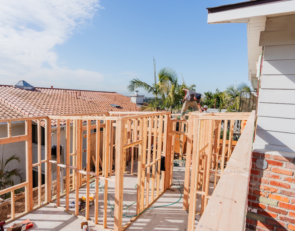 Framework of an ADU construction site with palm trees in a residential neighborhood, representing the impact of California ADU laws on HOA-regulated properties.