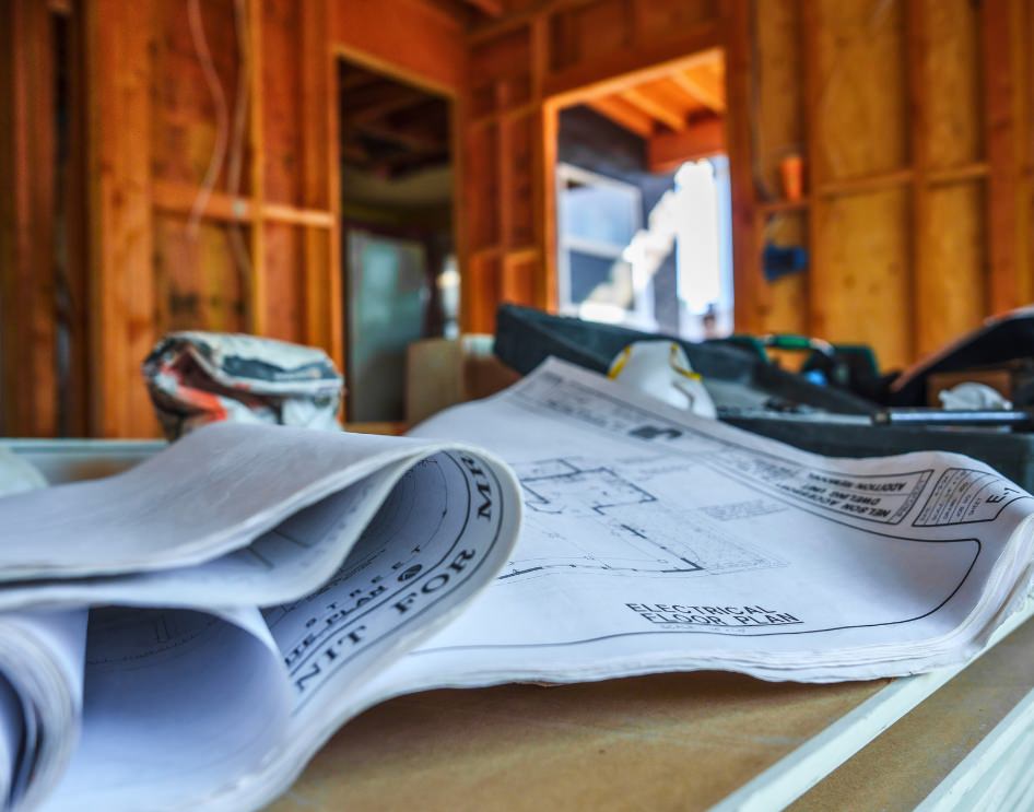 Close-up of blueprints and construction tools on a workbench inside a home under construction, symbolizing the need for detailed planning to meet HOA guidelines.