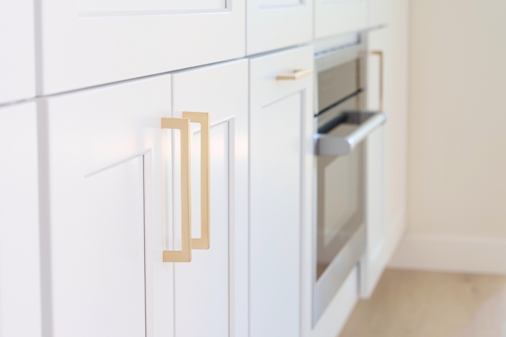 Close-up of white kitchen cabinetry with gold hardware and integrated stainless steel appliances in an ADU.