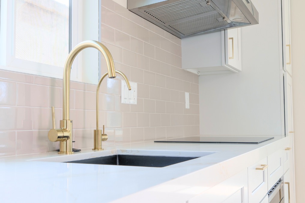 Modern kitchen sink with sleek gold faucets and glossy tile backsplash in a detached ADU.