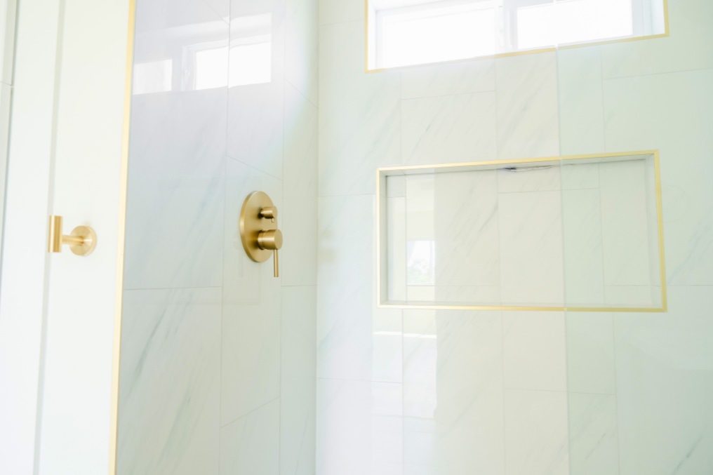 Modern ADU bathroom shower featuring marble tile walls, niche shelving, and gold hardware.