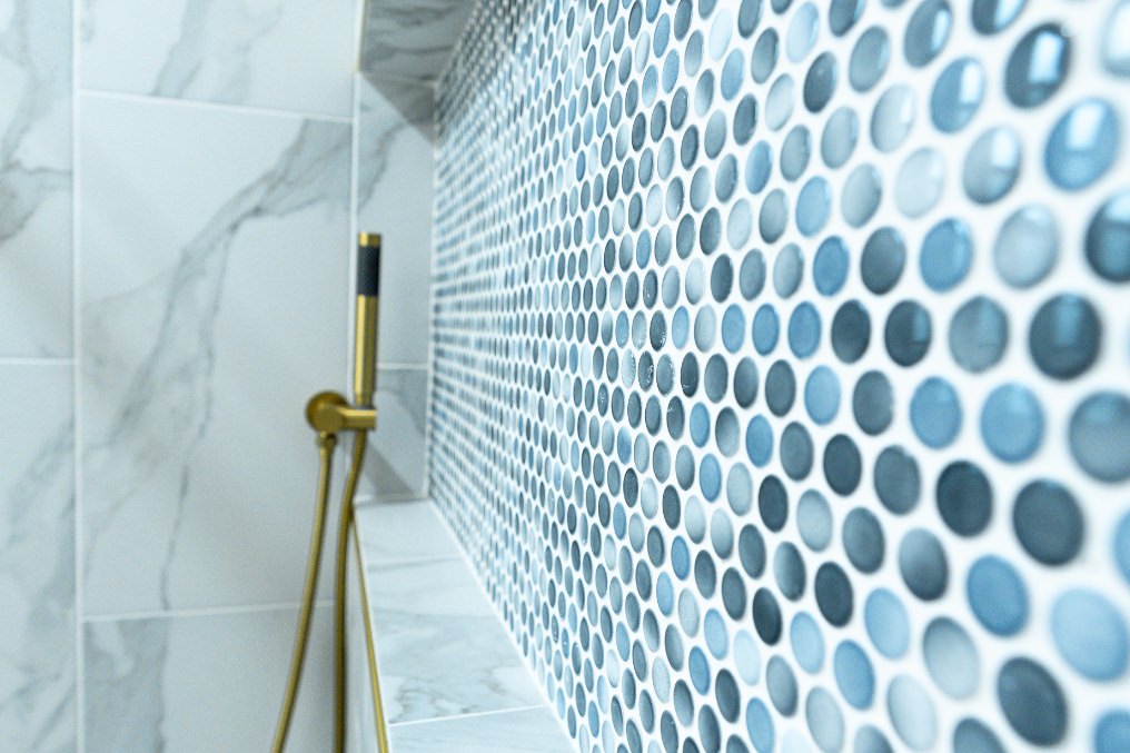 Detailed view of stylish blue mosaic tile work in ADU shower area, complemented by gold fixtures.