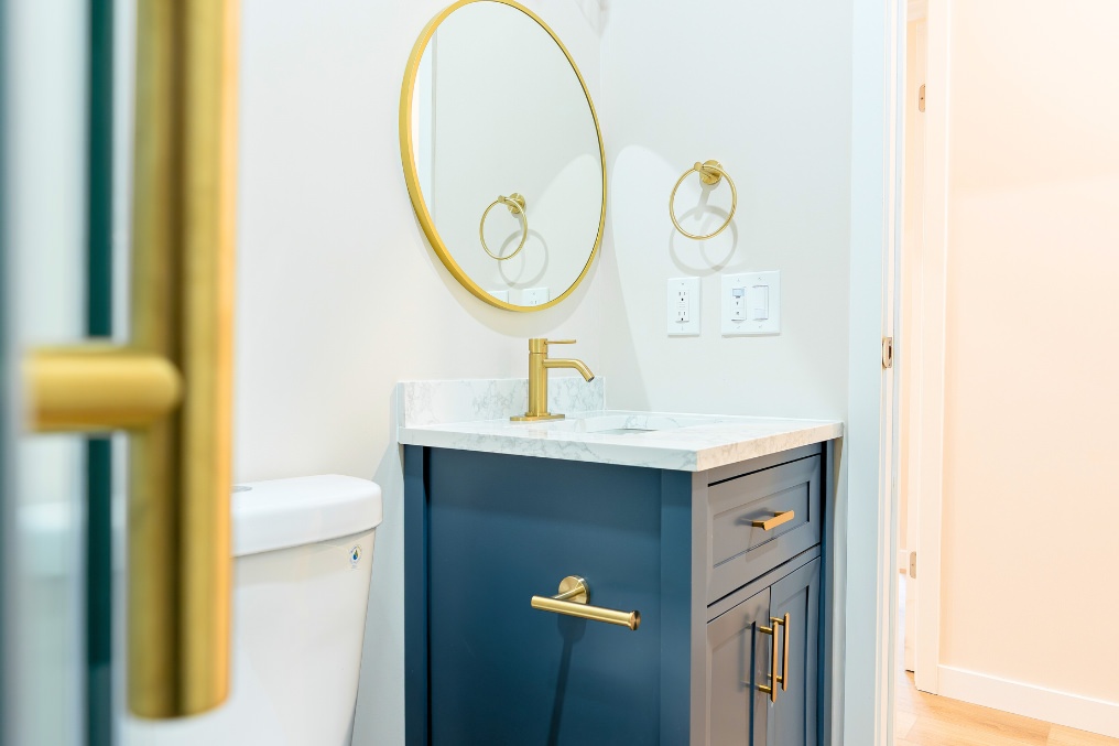 Modern bathroom vanity featuring blue cabinetry, gold fixtures, round mirror, and stylish marble countertop.