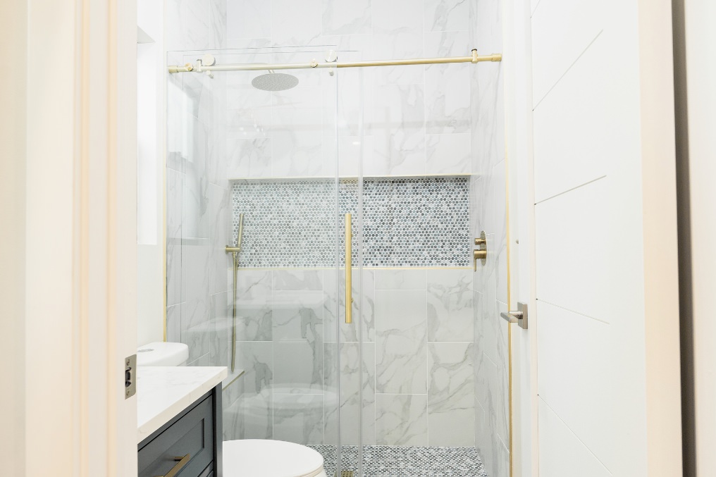 Modern ADU bathroom showcasing luxurious marble tile, glass shower enclosure, and gold fixtures.
