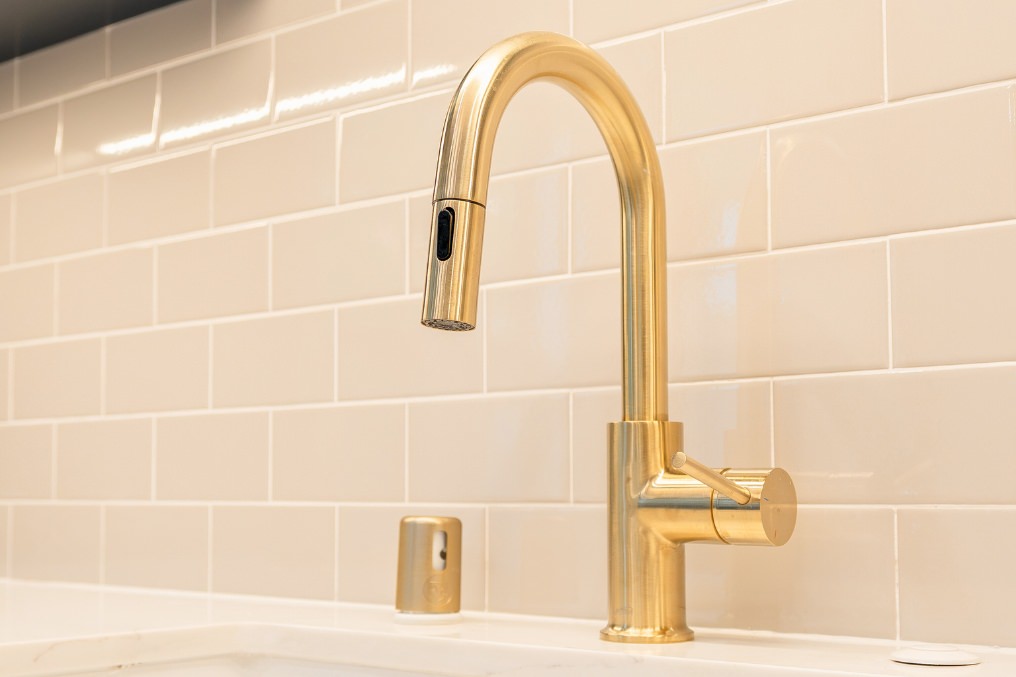 Close-up view of sophisticated gold kitchen faucet against a crisp white subway tile backsplash in modern ADU kitchen.