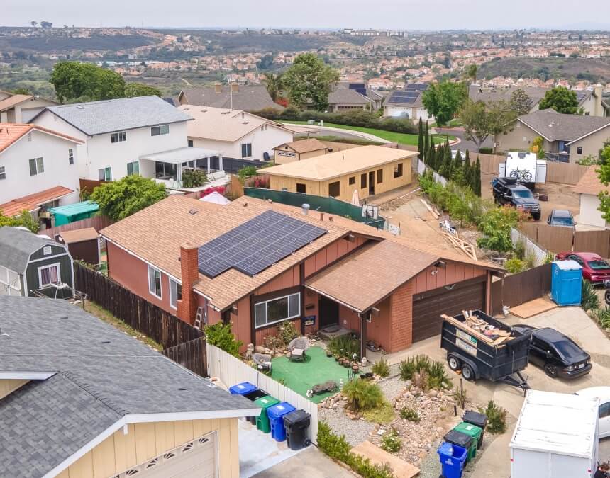 Wide-angle aerial view of a residential property with a large solar array and a new ADU being roofed, surrounded by greenery.