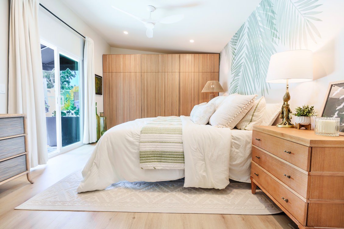 Contemporary ADU bedroom with wood-paneled closet wall, palm leaf accent wallpaper, and sliding glass door