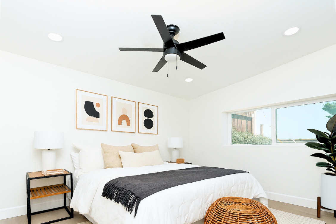 Minimalist ADU bedroom with black ceiling fan, abstract wall art, and neutral bedding