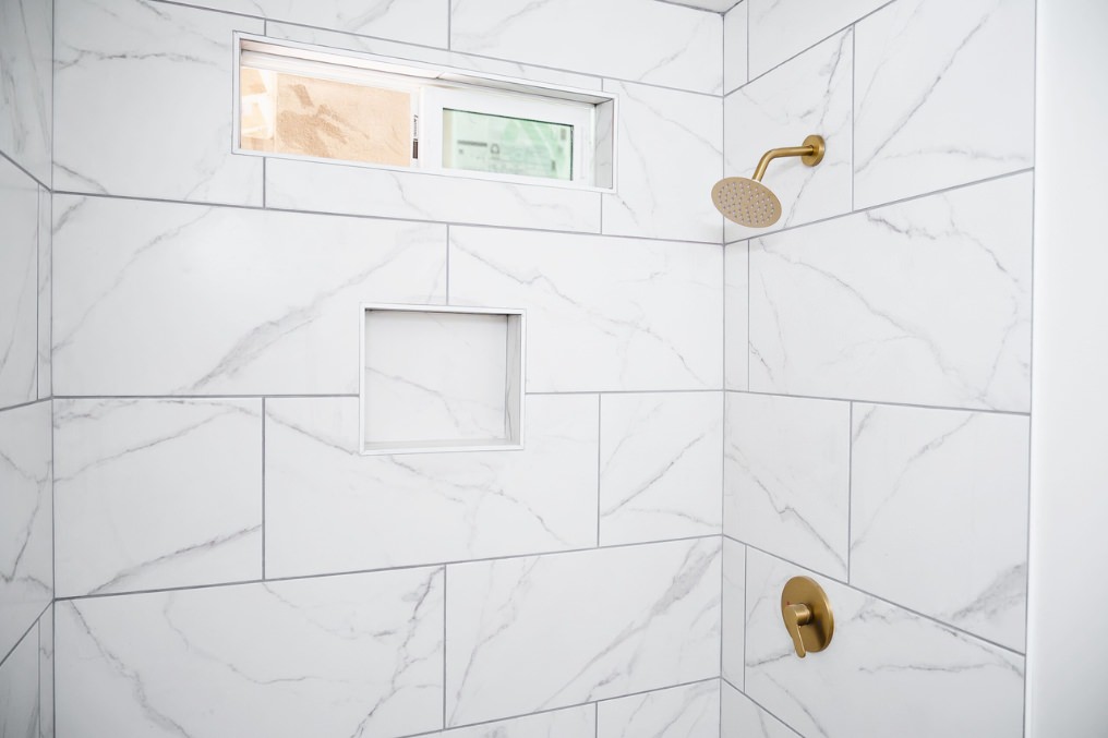 Modern tiled shower with gold fixtures in coastal-themed garage conversion bathroom.
