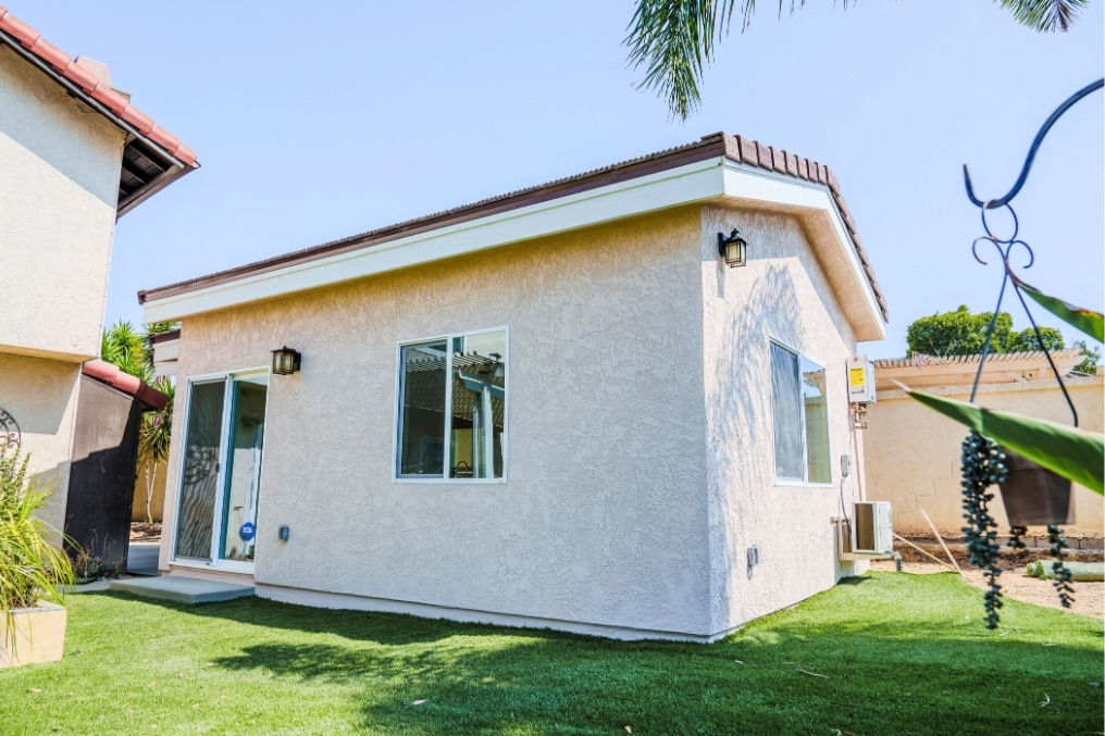 Exterior view of a stylish detached ADU with modern coastal design, sliding glass entrance, and lush green landscaping.