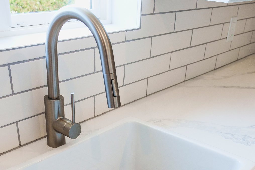 Close-up of brushed nickel kitchen faucet and modern sink, emphasizing clean, coastal aesthetics