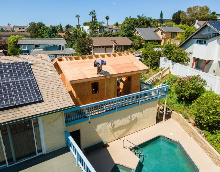 Rooftop view of an ADU being constructed beside a pool, adjacent to a home with solar panels.