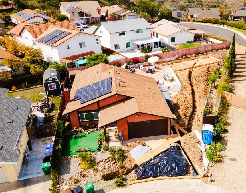 Backyard view of a solar-ready ADU under construction with nearby homes featuring rooftop solar panels.