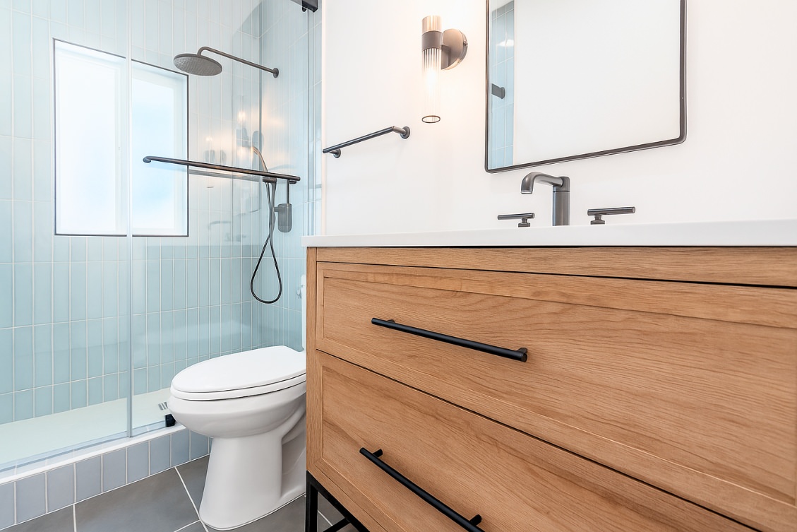 Minimalist ADU bathroom with light wood vanity, black hardware, and vertical subway tile shower