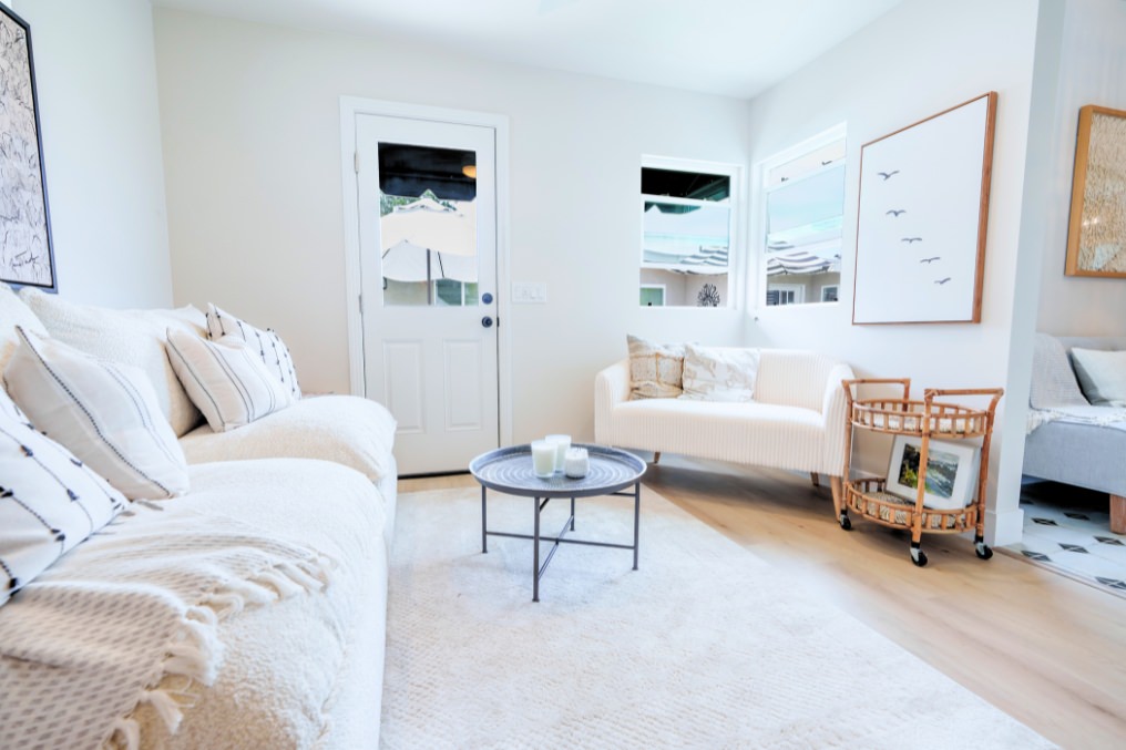 Bright ADU living room with white sofas, light wood floors, and cozy neutral décor